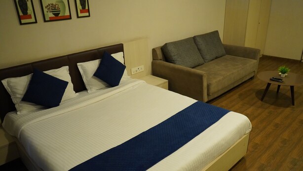 A hotel room with a large bed, a sofa, a small table, and a wall-mounted power outlet. - Wow Studio at Weekend Address (Surat)