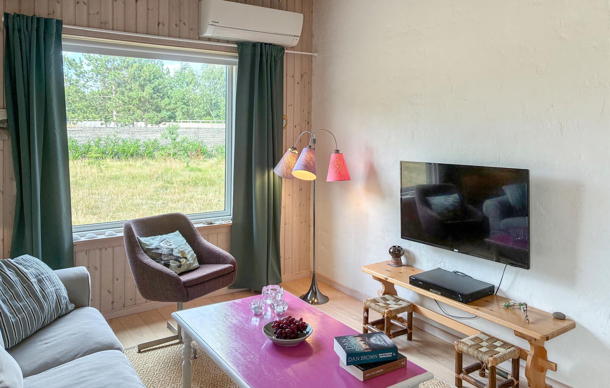 A living room with a sofa, a table with a bowl of fruit and a book, a floor lamp, a TV, and a window with curtains.