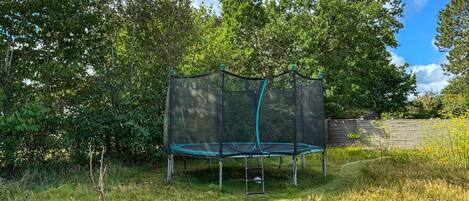 A trampoline with a safety net in a grassy area with trees in the background.