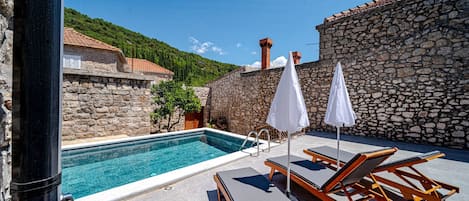 A pool area with stone walls, lounge chairs, and umbrellas.