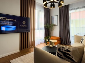 A modern living room with a flat-screen TV mounted on the wall, a round orange sofa, a beige armchair, and a small round table with a plant. - "Onyx" – Adults Only (+16) (Saranda)