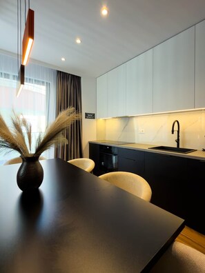 A modern kitchen with a dark countertop, a black sink, and white cabinets. There is a vase with dried plants on the table. - "Onyx" – Adults Only (+16) (Saranda)