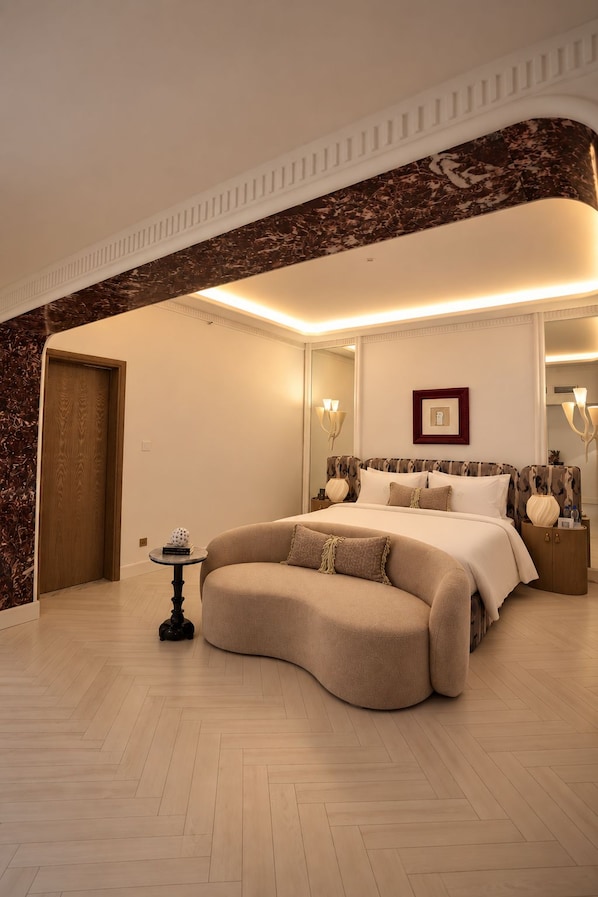 A spacious bedroom with a curved sofa, a large bed, and a mirror. - Nishat Hotel Margala (Islamabad)