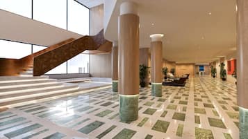 A spacious lobby with a staircase, large pillars, and a patterned floor.