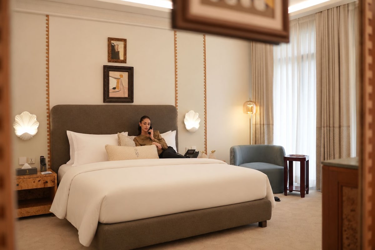 A hotel room with a large bed, a bedside table, a chair, and a lamp.