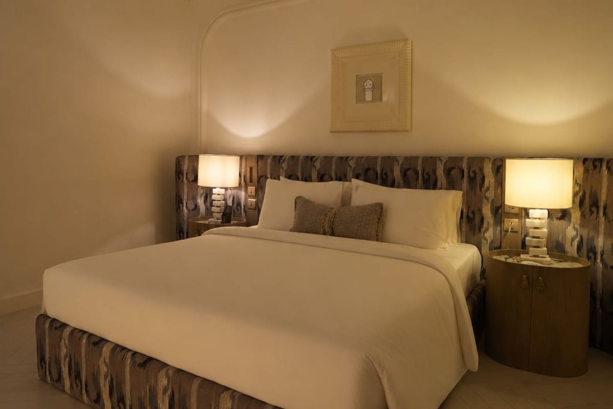 A large bed with a patterned headboard, two bedside lamps, and a framed picture on the wall.
