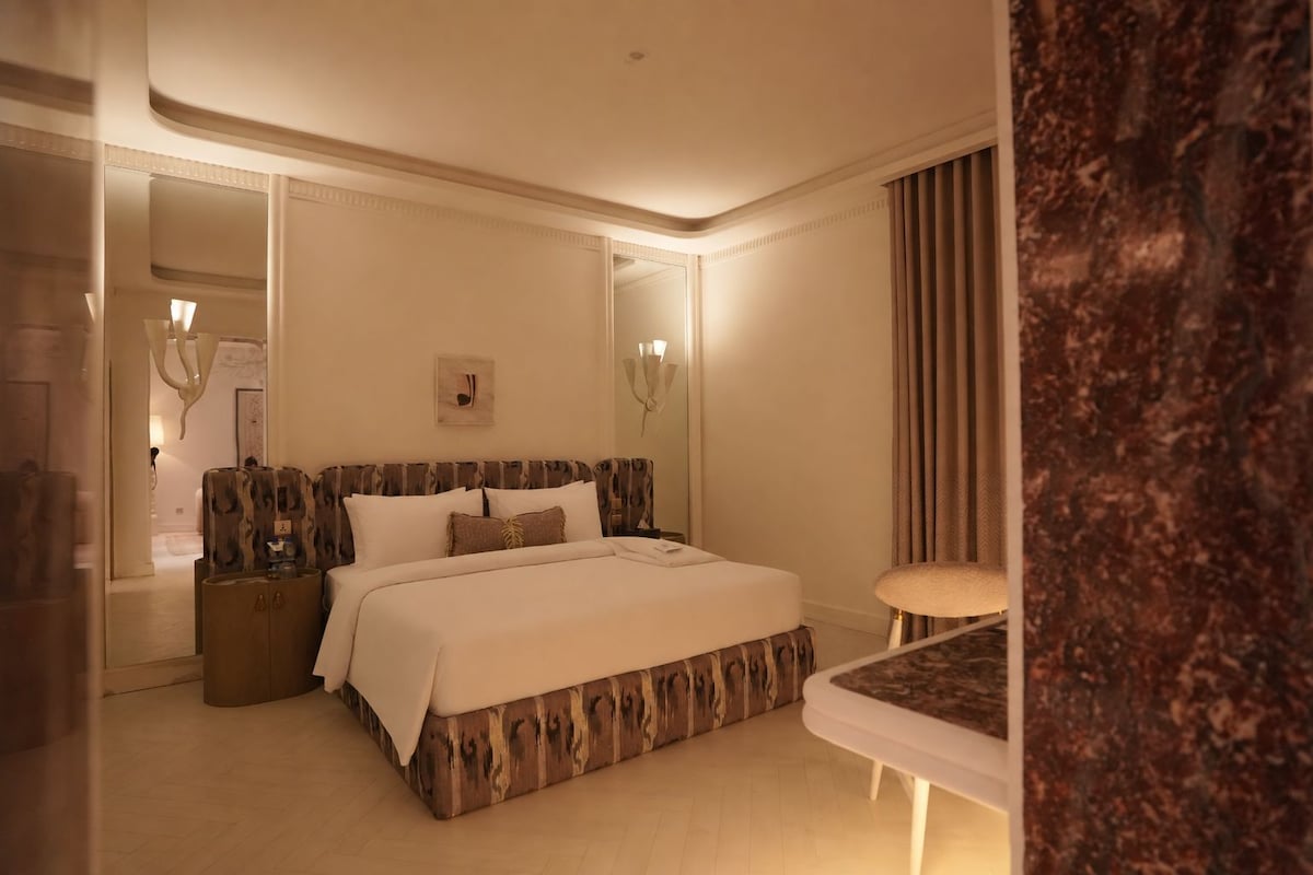 A hotel room with a large bed, bedside tables, a mirror, and a small seating area.