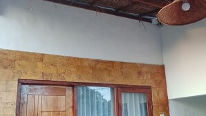 Una habitación con puerta de madera, ventana, techo de paja y pared de piedra.