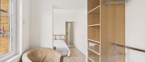 A bedroom with a bed, a chair, a wardrobe with shelves, and a window.