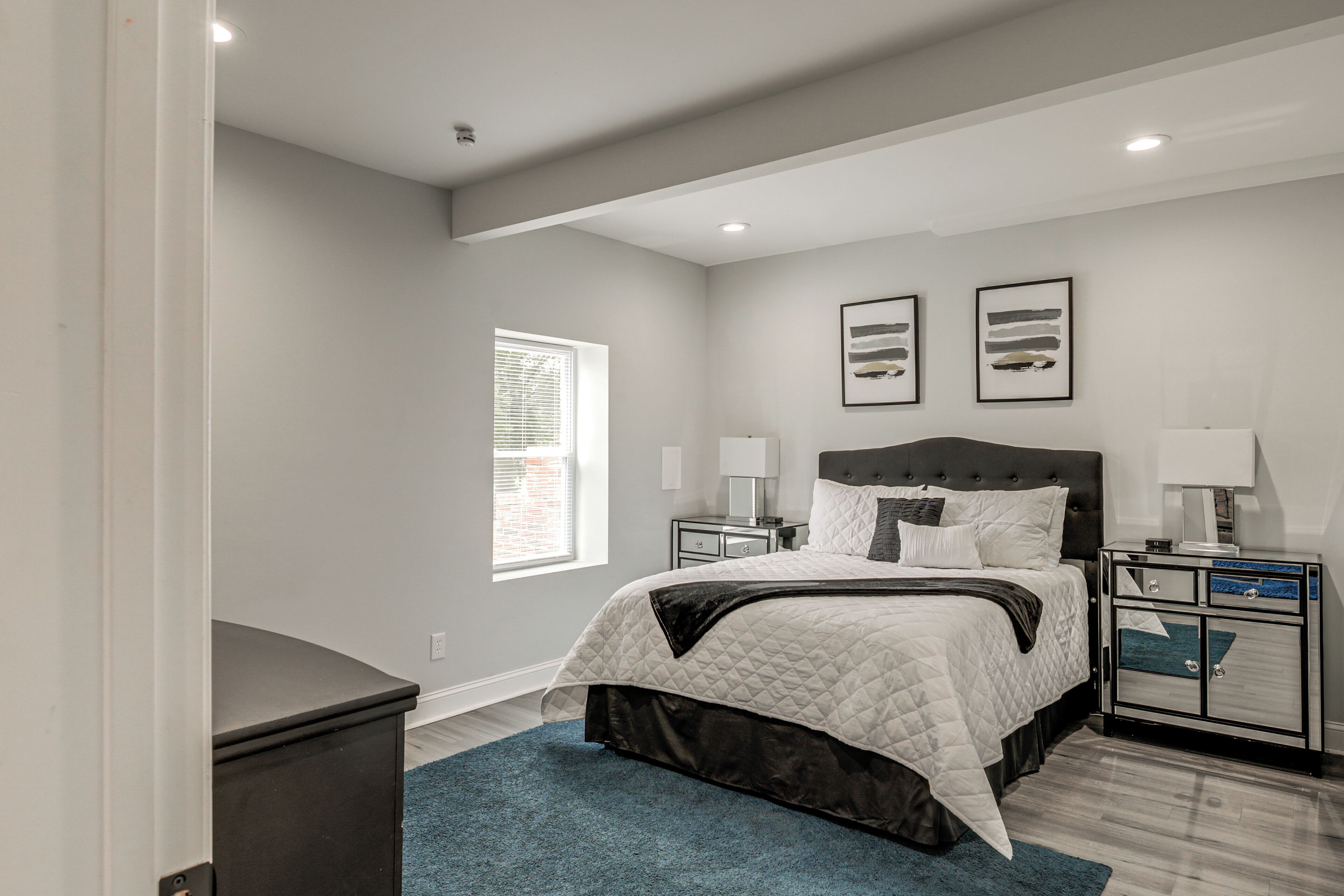 Un dormitorio con cama, mesitas de noche, cómoda, ventana y decoración en la pared.