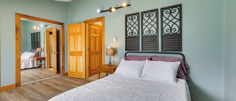 A bedroom with a large bed, a wooden door, a mirror, and a wall-mounted light fixture.