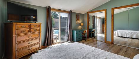 A bedroom with a large bed, a dresser, a desk, and a sliding glass door leading to a balcony.