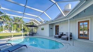 A covered swimming pool area with lounge chairs and a patio table. - Modern 2-unit Combo w/ Pool: 'naples Hideaway' (Naples)