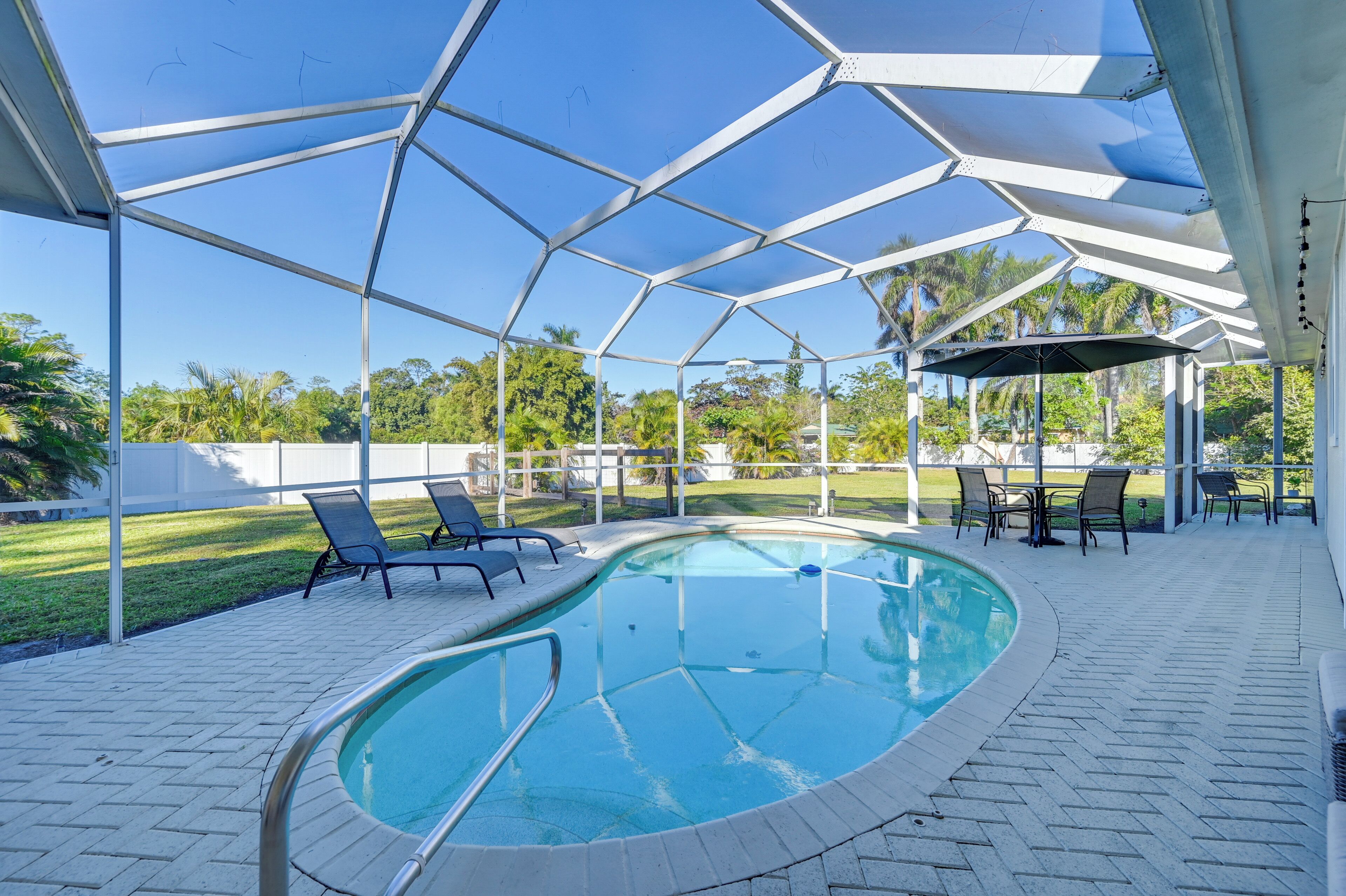 Una piscina exterior techada con sillones y mesas, rodeada por una estructura de metal blanco y un cielo azul cristalino.