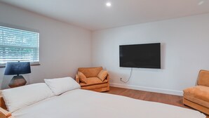 A bedroom with a bed, two armchairs, a TV mounted on the wall, and a window with blinds. - Modern 2-unit Combo w/ Pool: 'naples Hideaway' (Naples)