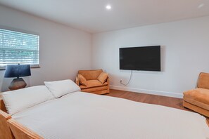 Ein Schlafzimmer mit einem Bett, zwei Sesseln, einem an der Wand befestigten Fernseher und einem Fenster mit Jalousien.