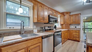 A kitchen with wooden cabinets, stainless steel appliances, a granite countertop, and a window with a view of greenery.