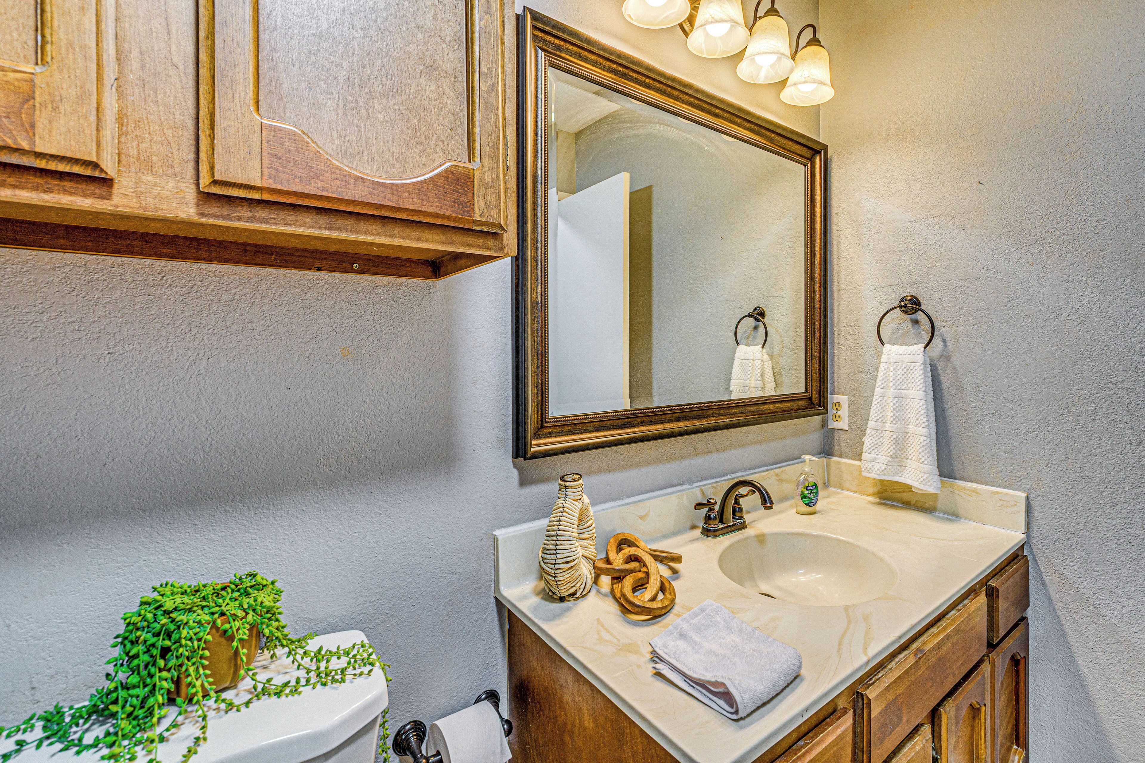 A bathroom with a marble sink, wooden cabinets, a mirror with lights, a toilet, and a potted plant.