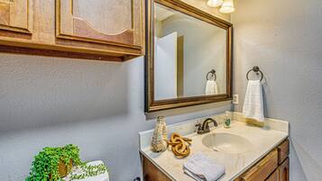 A bathroom with a marble sink, wooden cabinets, a mirror with lights, a toilet, and a potted plant.