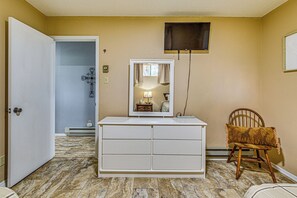 A room with a white dresser, a chair with a giraffe-patterned cushion, a mirror, and a wall-mounted television. - Shuffleboard & Arcade! Alto Family Escape (Alto)