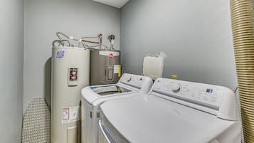 Zona de lavandería con lavadora y secadora de pared, un extractor de aire y un cartel de seguridad.