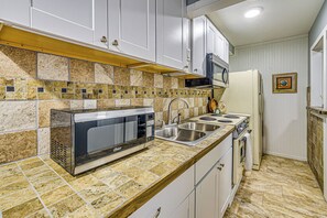 Una cocina con microondas, estufa, fregadero y salpicadero de azulejos.