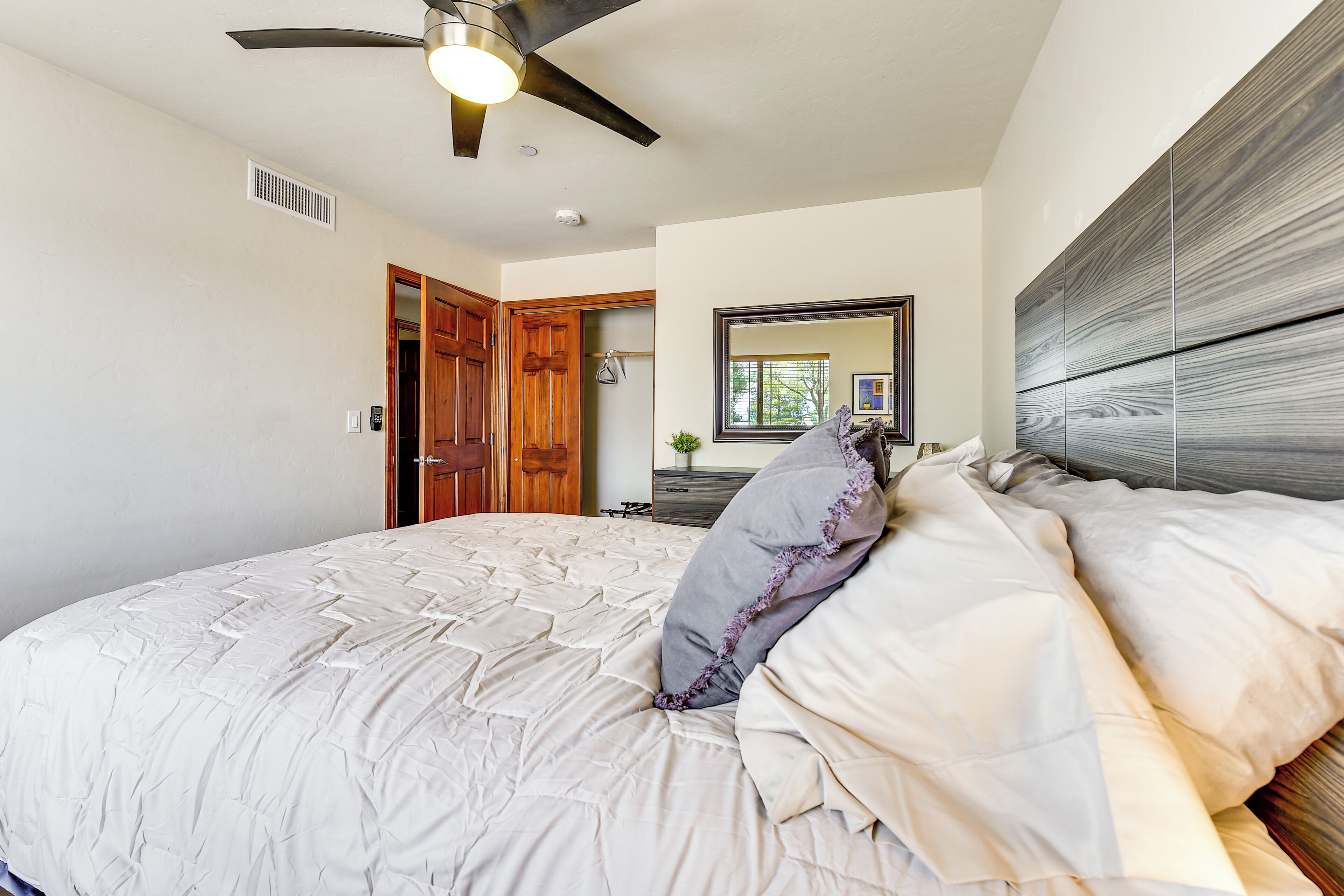 A bedroom with a bed, a ceiling fan, a wooden door, a mirror, and a dresser.