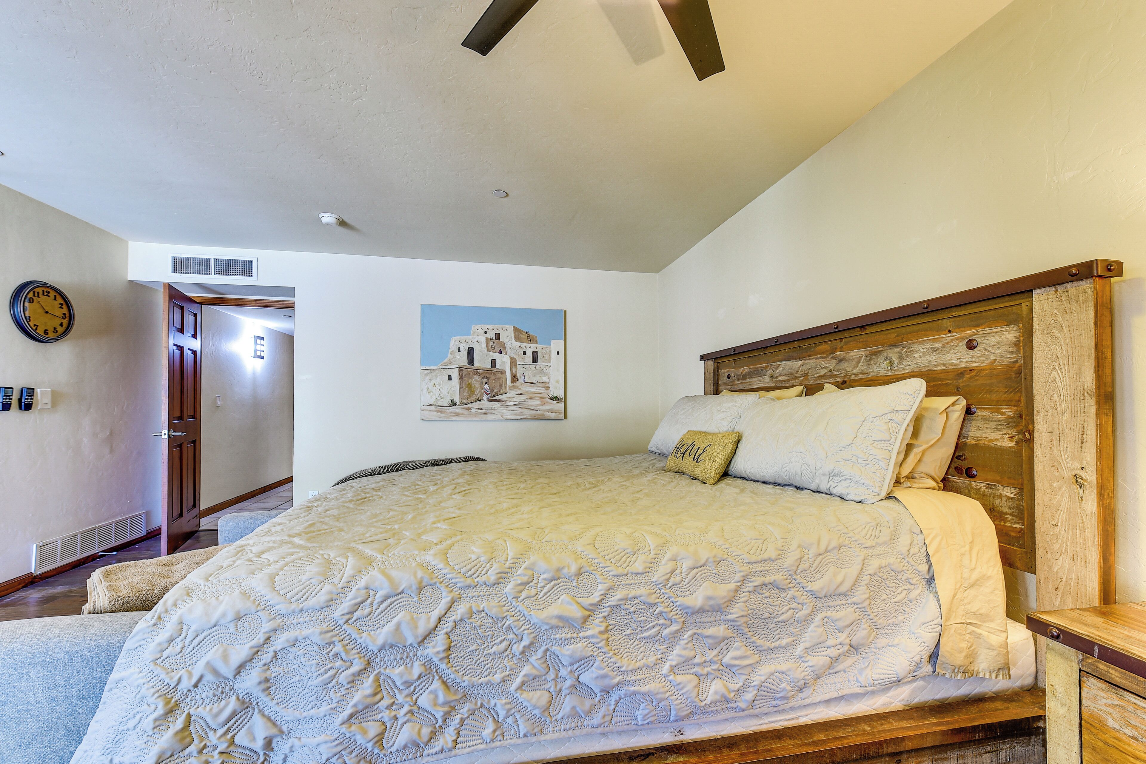 A bedroom with a large bed, a wooden headboard, a wall clock, and a painting.