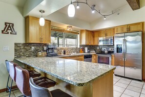 A kitchen with wooden cabinets, a stainless steel refrigerator, granite countertops, and bar stools. - Game Room, Playset! Family-friendly Tucson Getaway (Tucson)