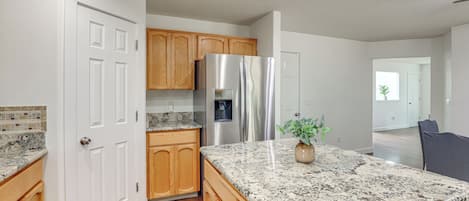 Cocina con gabinetes de madera, refrigerador de acero inoxidable, encimeras de granito y una planta en maceta.