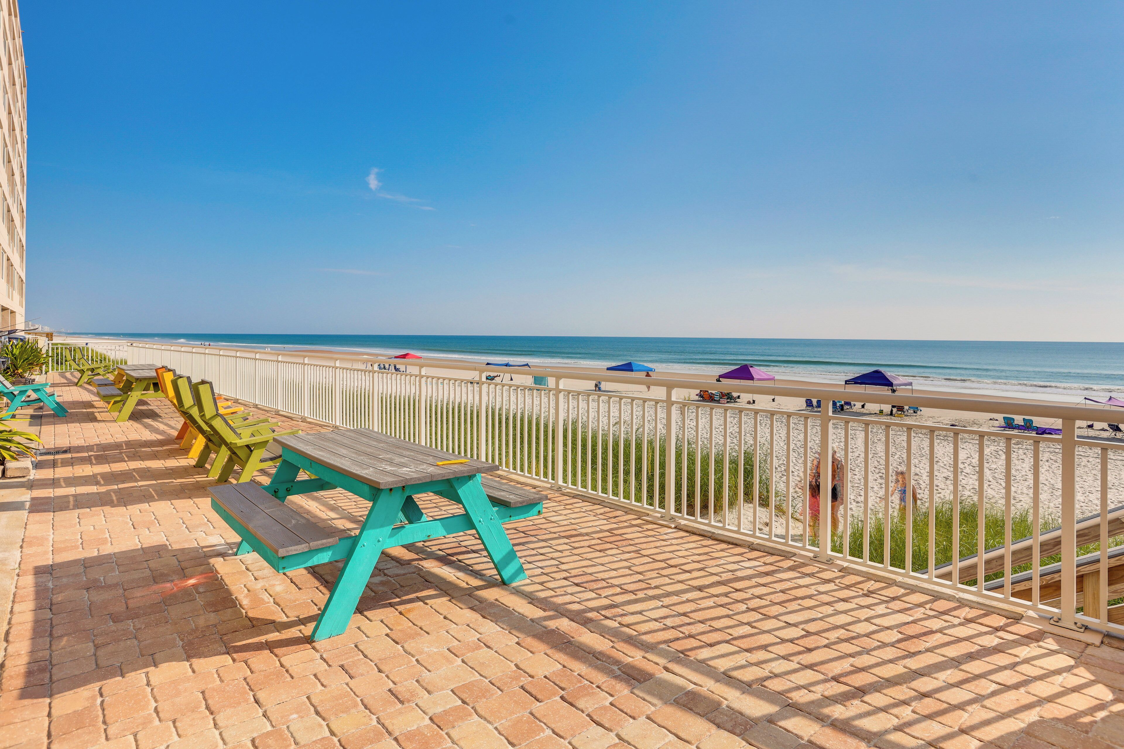 A seaside balcony with a picnic table and chairs, overlooking the beach and ocean.