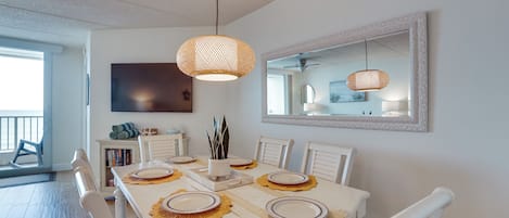 A dining area with a long table, white chairs, and a ceiling fan.