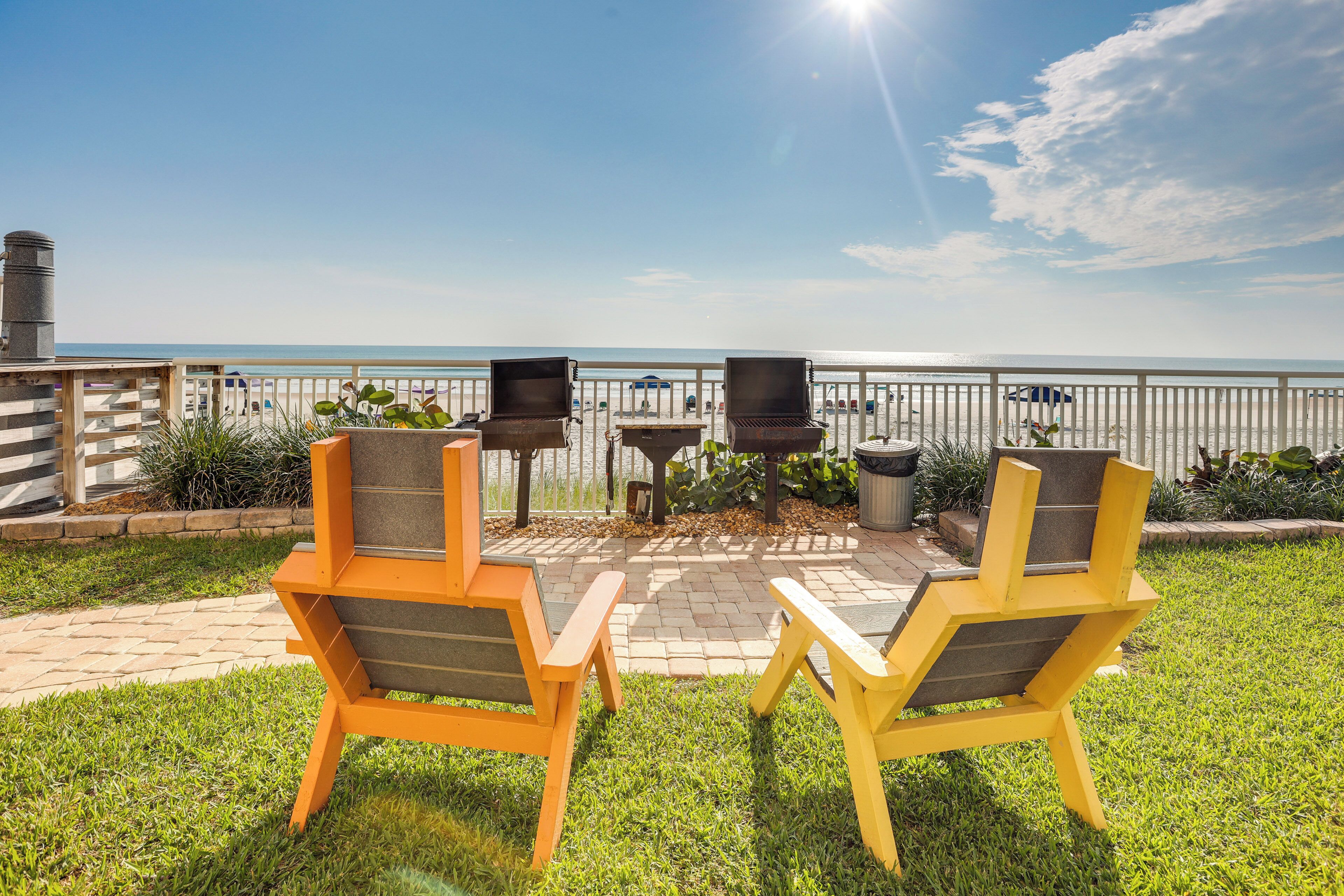 A patio with two yellow chairs, a grill, and a view of the beach.
