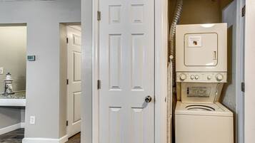 A laundry room with a stacked washer and dryer, a door with a handle, and a wall-mounted thermostat.