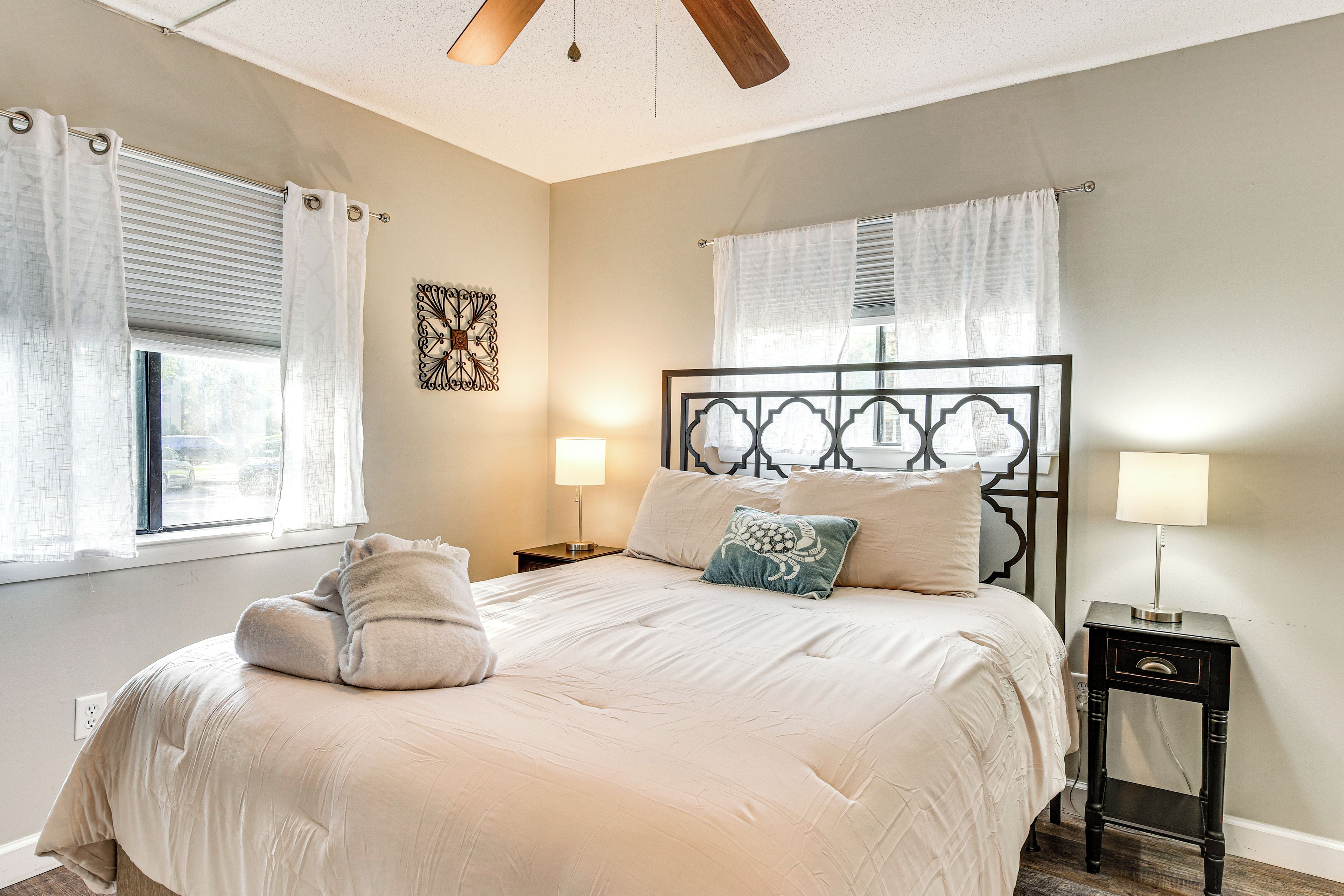 A bedroom with a bed, two bedside tables, a ceiling fan, and a window with curtains.