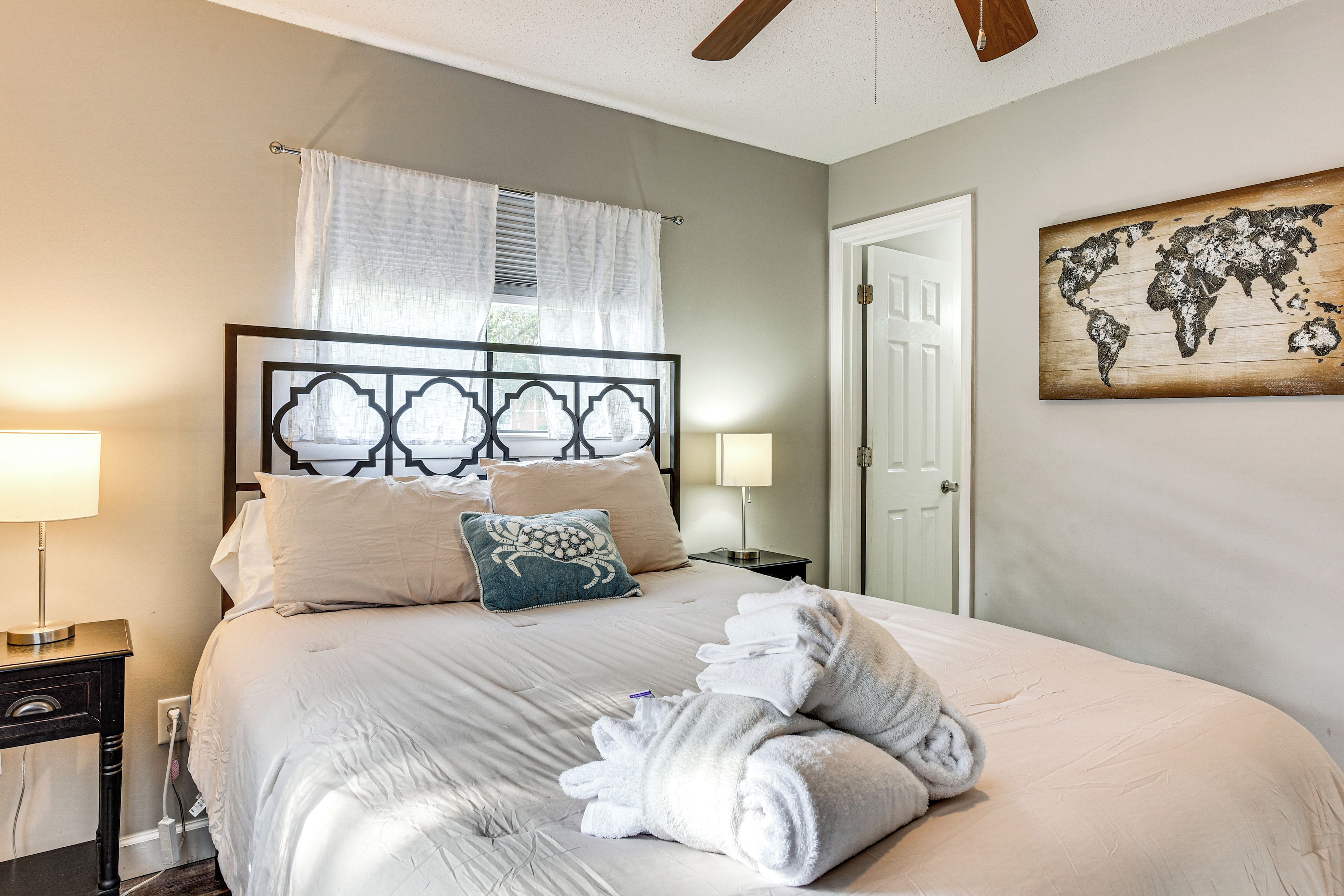 A hotel room with a bed, two bedside lamps, a world map artwork, and a door.