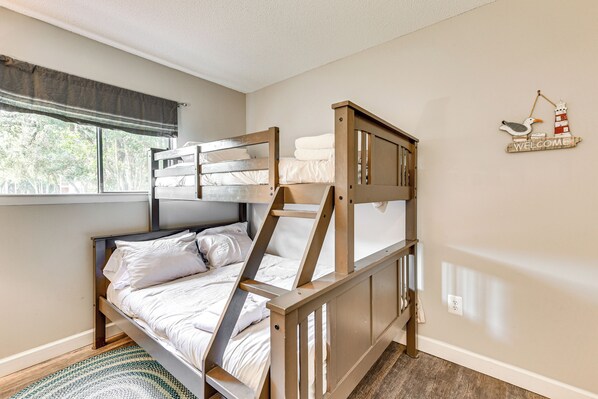 A bunk bed with a ladder, a window with a view of trees, and a welcome sign with a lighthouse and seagull. - Unwind Poolside, Walk to Beach! Tennis, Pickleball (Hilton Head Island)