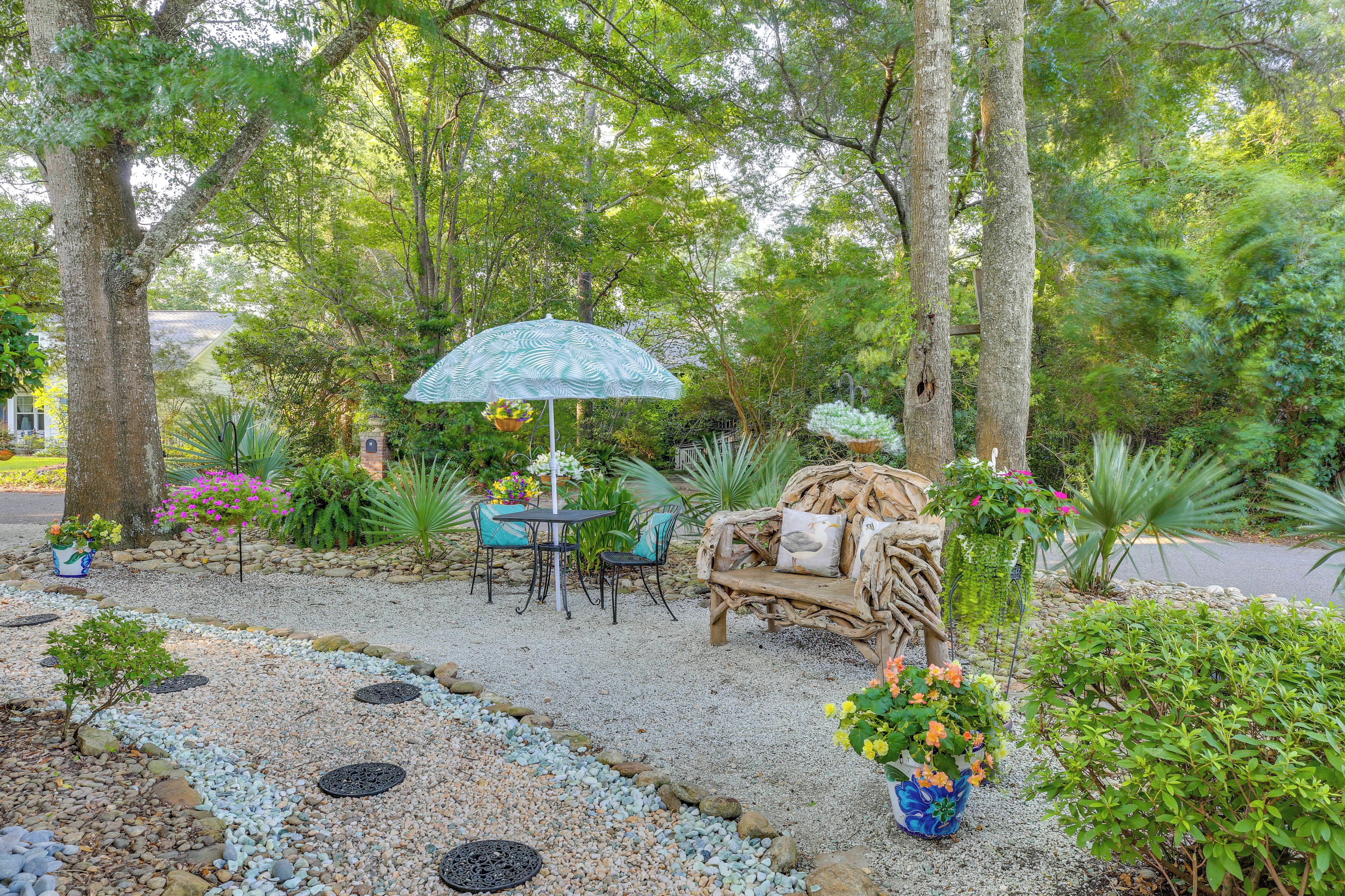 A garden patio with a table and chairs, a wicker bench, and a decorative umbrella.