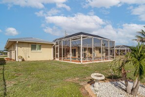 Ein Haus mit einer großen, verglasten Veranda, einem eingezäunten Garten und einem kleinen Garten mit Vogeltränke.
