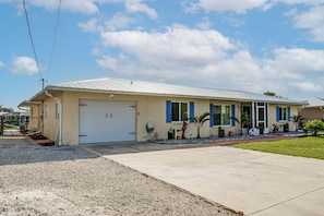 A single-story house with a garage, a front yard with gravel and plants, and a clear sky. - Pool, Fishing Dock! Port Charlotte Canal-front Gem (Port Charlotte)