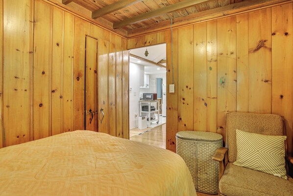 Una habitación con paneles de madera, una cama, una silla y un cesto de basura.