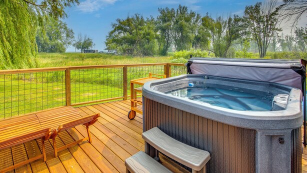 Un jacuzzi en una terraza de madera con vistas a un campo cubierto de césped y árboles.