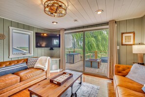 A cozy living room with a leather sofa, a wooden coffee table, and a large window offering a view of the outdoors. - Bayfront Home! Dock, Deck, Hot Tub, & Fire Pit (Oconto)