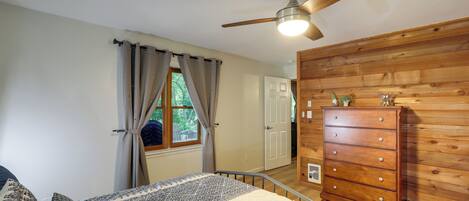 Un dormitorio con cama, ventilador de techo, cómoda de madera y ventana con cortinas.