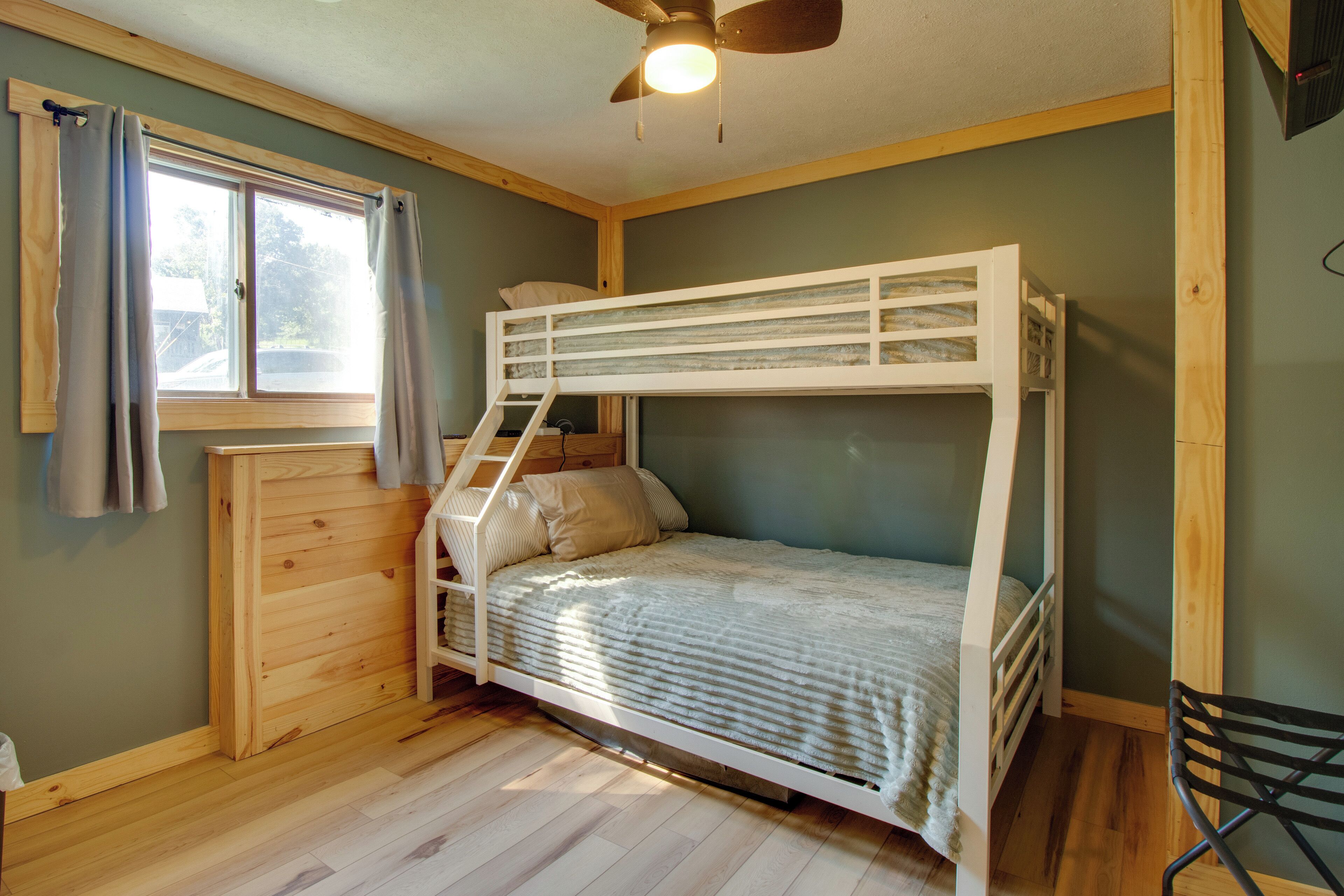 A bunk bed room with a window, wooden walls, and a ceiling fan.