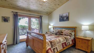 Un dormitorio con una cama de madera, una mesita de noche con lámpara, un aparador, una puerta al balcón y un ventilador de techo.