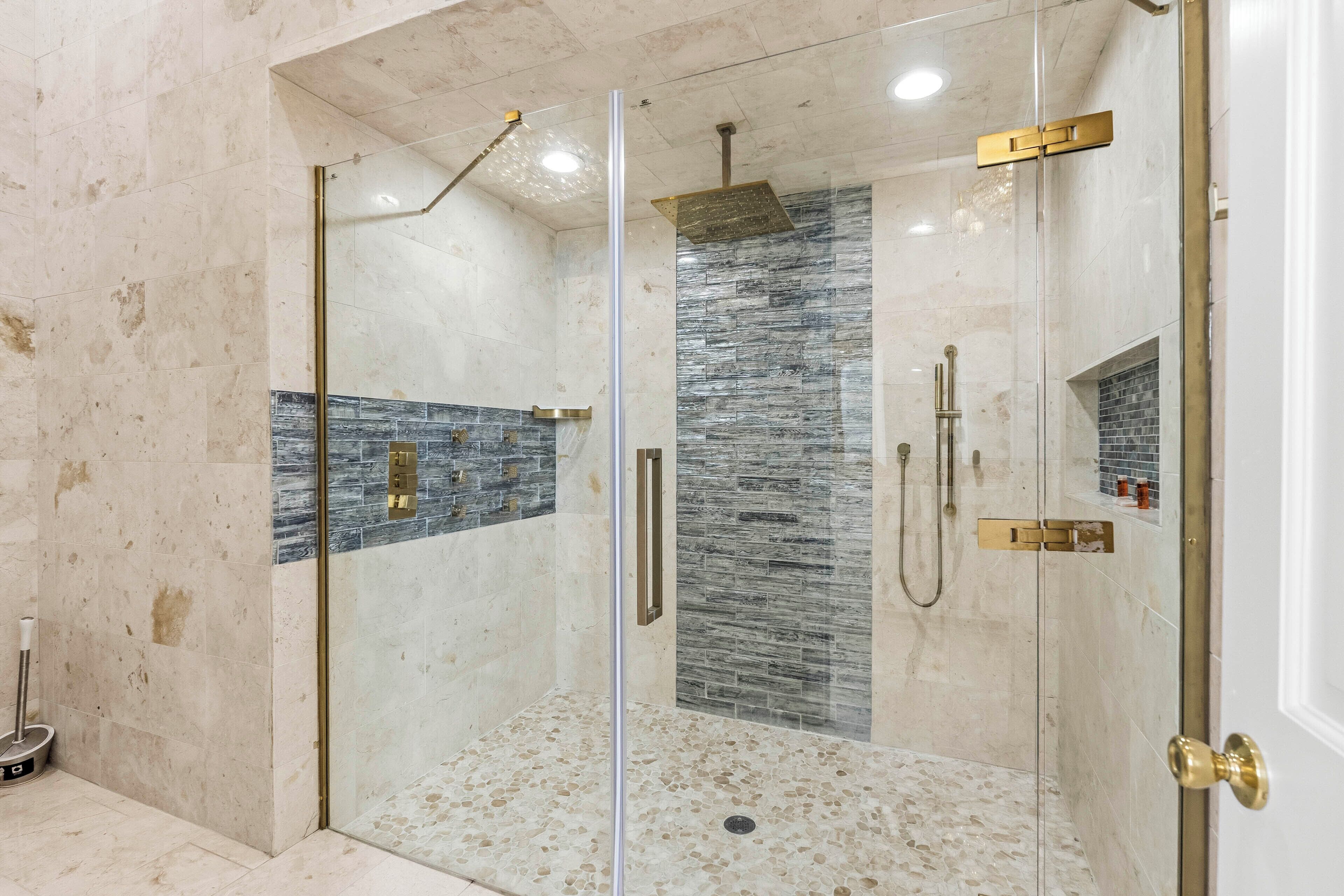 A glass-enclosed shower with a stone mosaic wall, a handheld showerhead, and a handheld shower attachment.