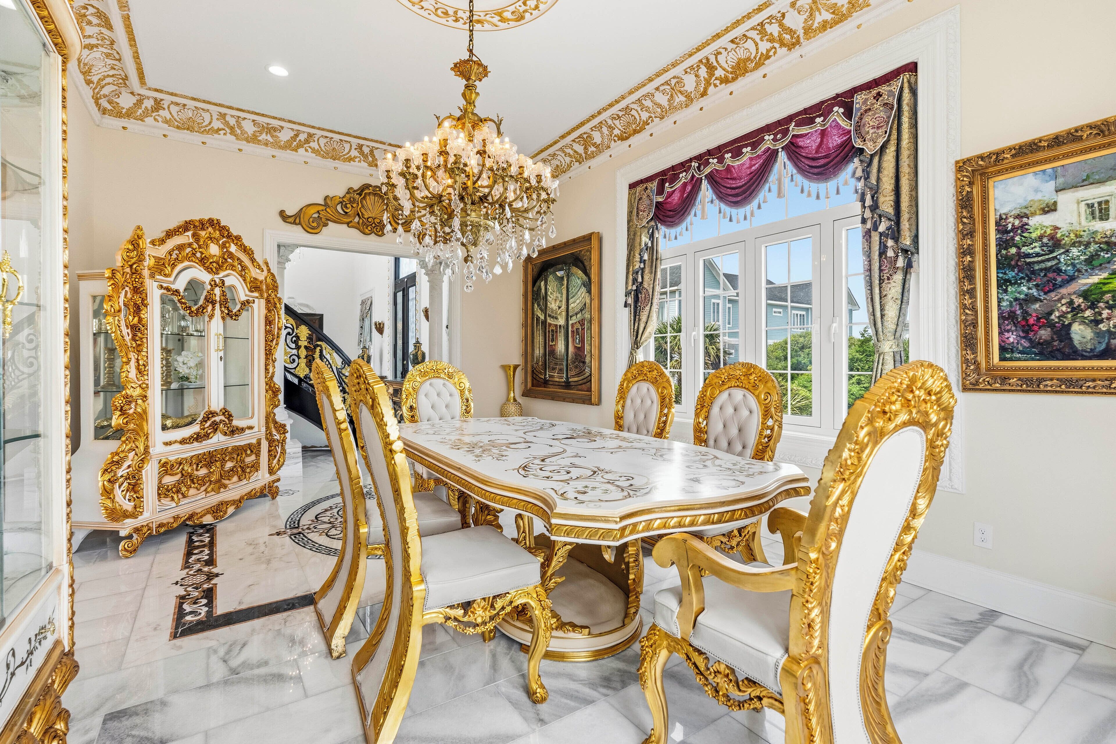 Un espace repas agrémenté d’une table en marbre, de chaises dorées et blanches, d’un lustre et de décorations raffinées.