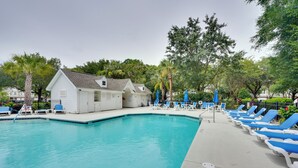 Piscina com espreguiçadeiras, um pequeno edifício e árvores ao fundo.