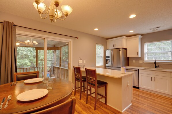 A modern kitchen with a central island, stainless steel appliances, and a dining area with a wooden table and chairs. - Charleston Townhome Near Credit One Stadium (Charleston)
